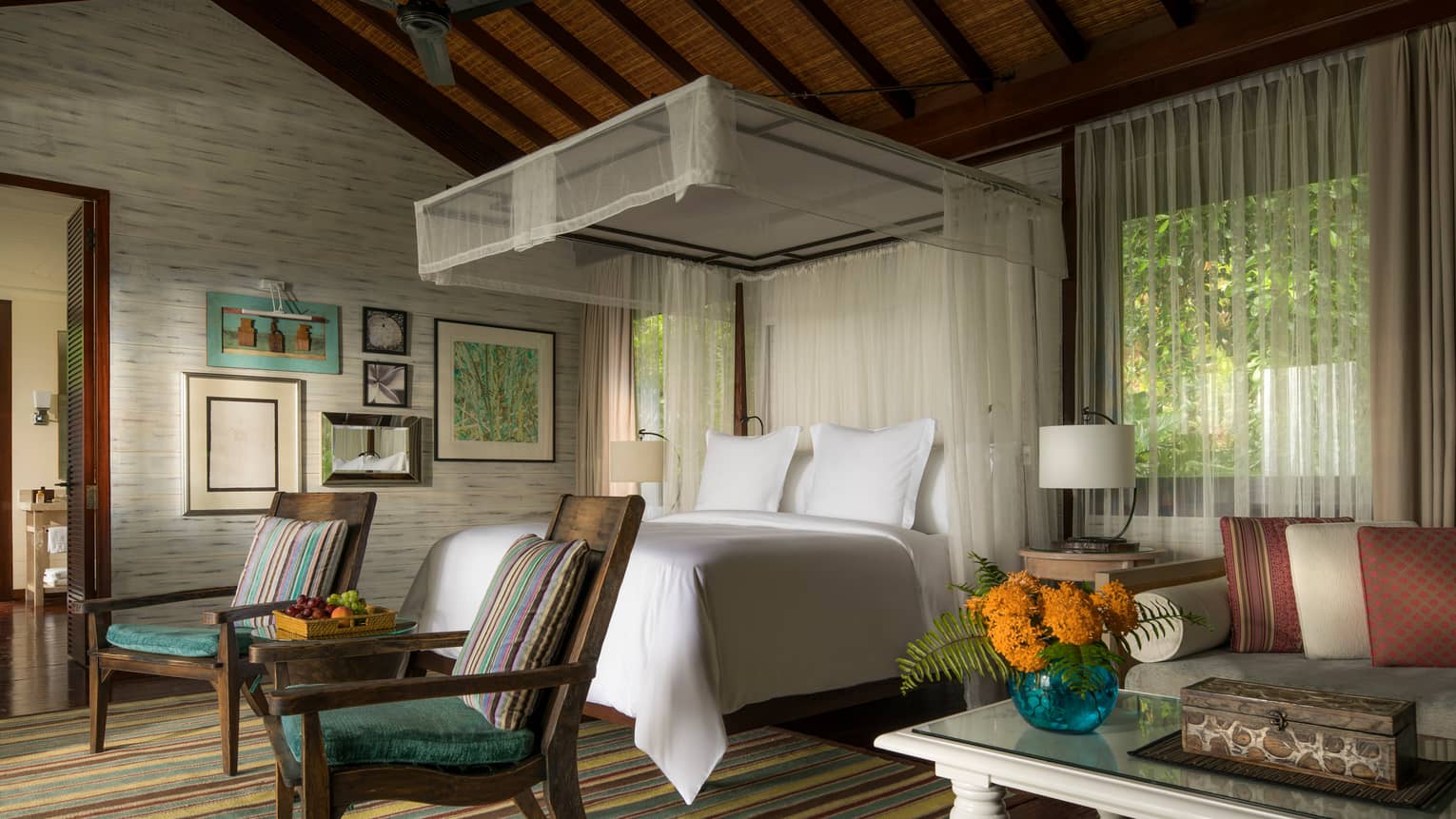 Suite with white canopied bed, two colourful striped chairs at foot, striped rug and sitting area