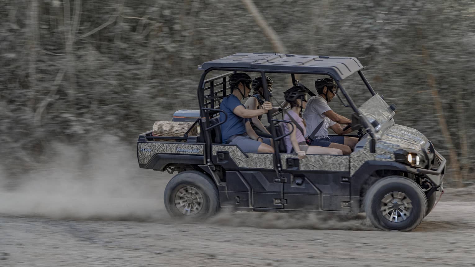 Four people speed along a dirt road in a 4x4 vehicle
