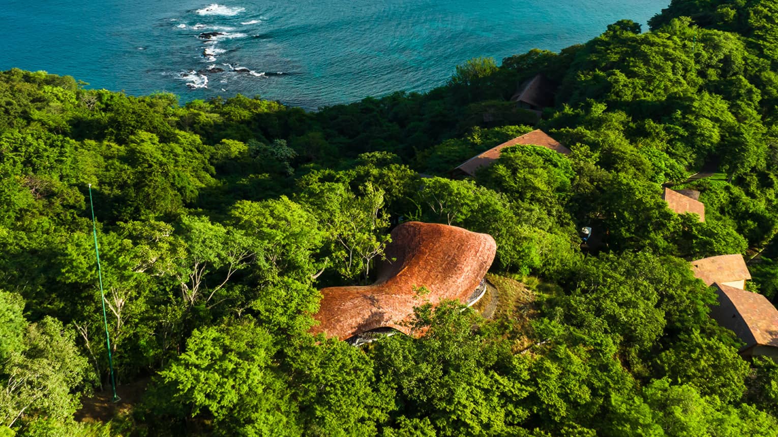 Aerial view of open-air Wellness Shala tucked between greenery on a hilltop overlooking the ocean