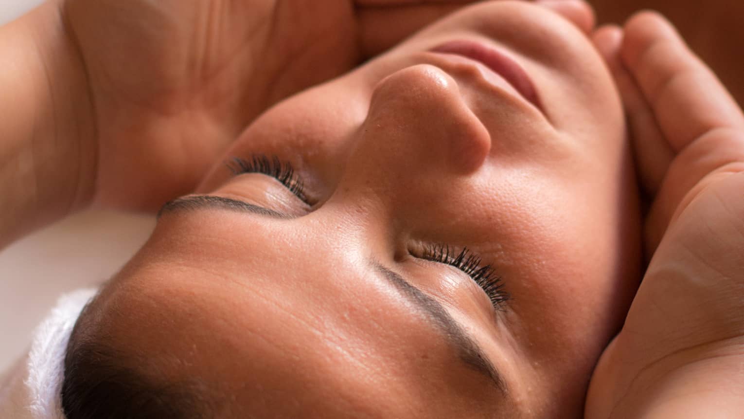 Close-up of woman with eyes closed facing up as hands cup her face and chin