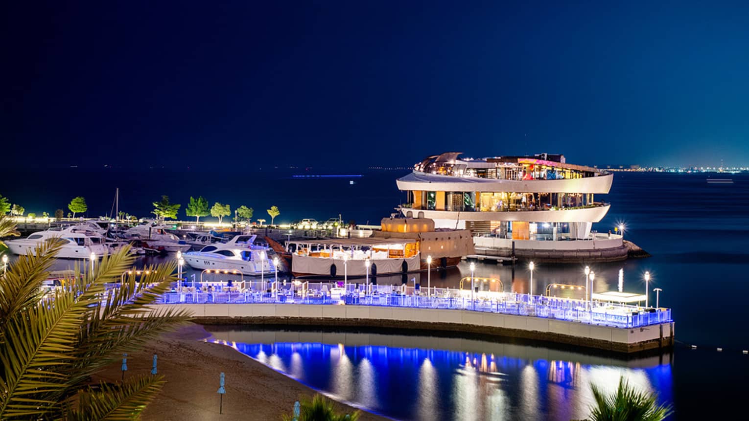 A dock covered in blue lights with a floating restaurant in the bay behind it.