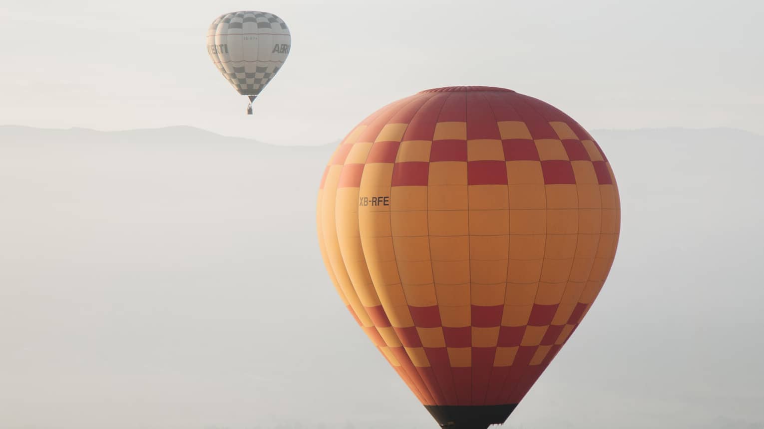 Yellow hot air balloon with red checkers in sky, hot air ballon in distance 
