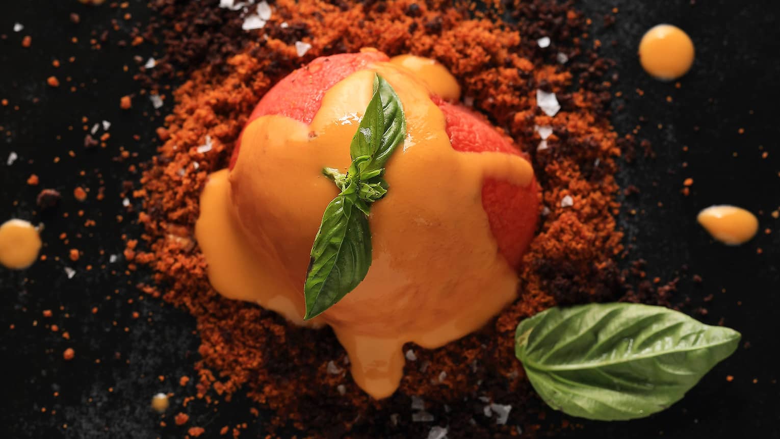 A close up of a orange sorbet like dish covered in an orange sauce and garnished with mint 