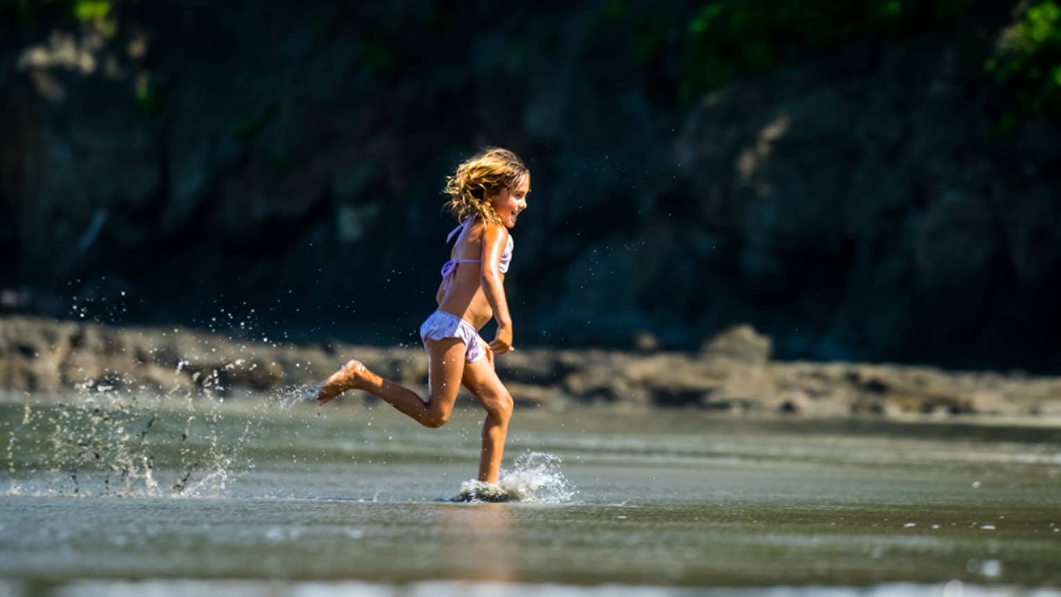 Young girl runs smiling through the shallow water along the beach