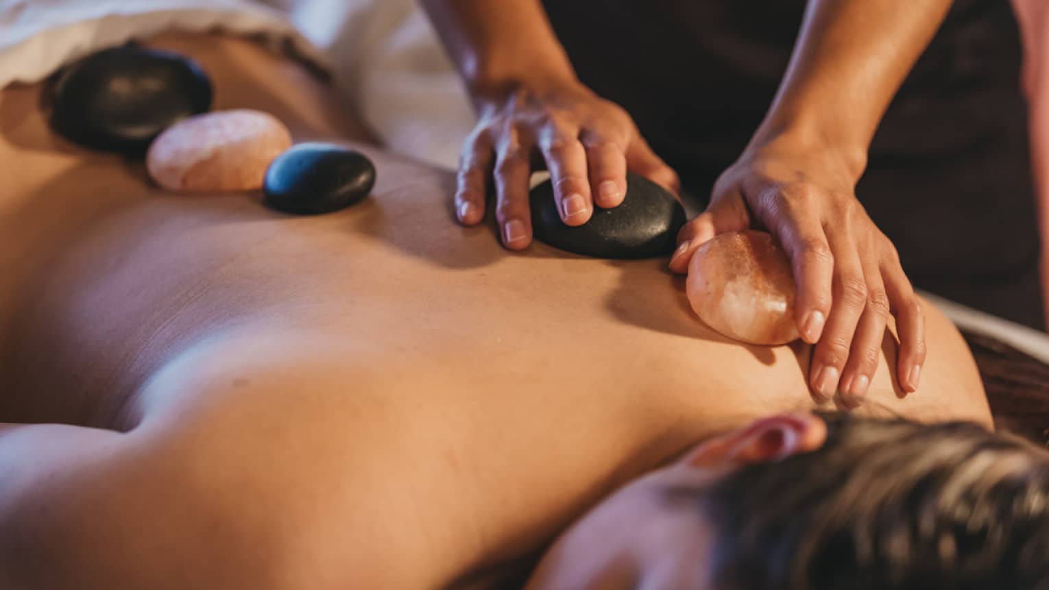 Close up of hands massaging warm stones on a woman's bare back