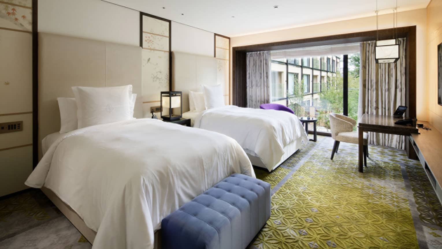 Bedroom with two twin beds, blue upholstered bench, desk and chair, and large window