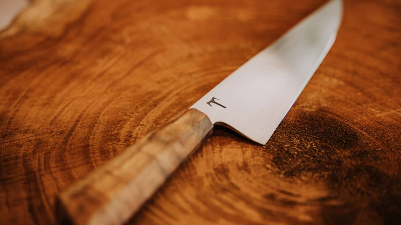 A custom chef's knife lies on a wooden table
