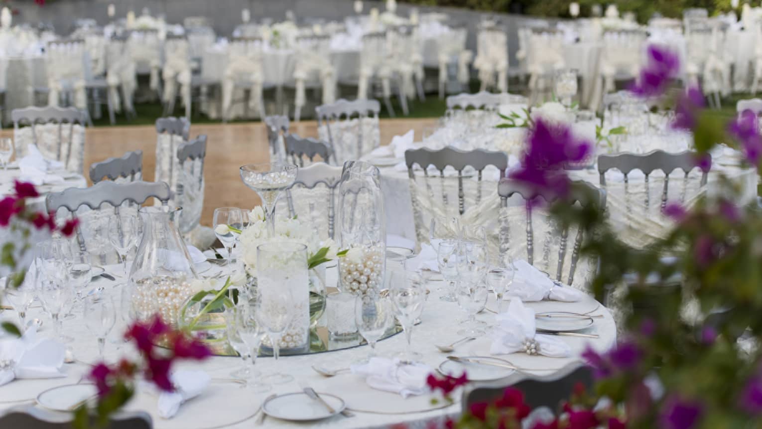 Outdoor banquet with round dining tables covered in crystal, pearl, floral decorations