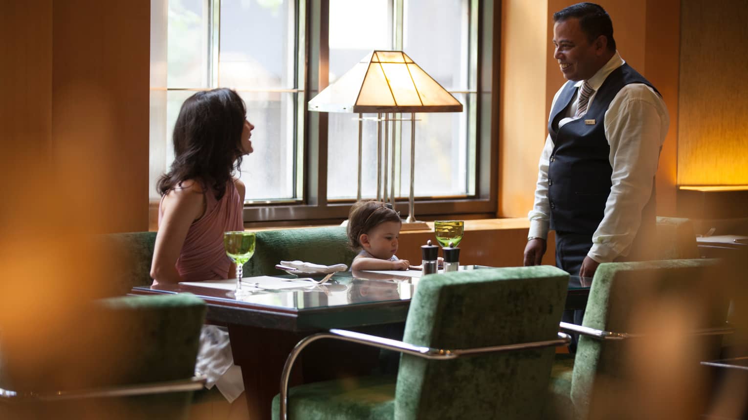 Garden Restaurant server stands by booth where woman, toddler sit on velvet green bench 