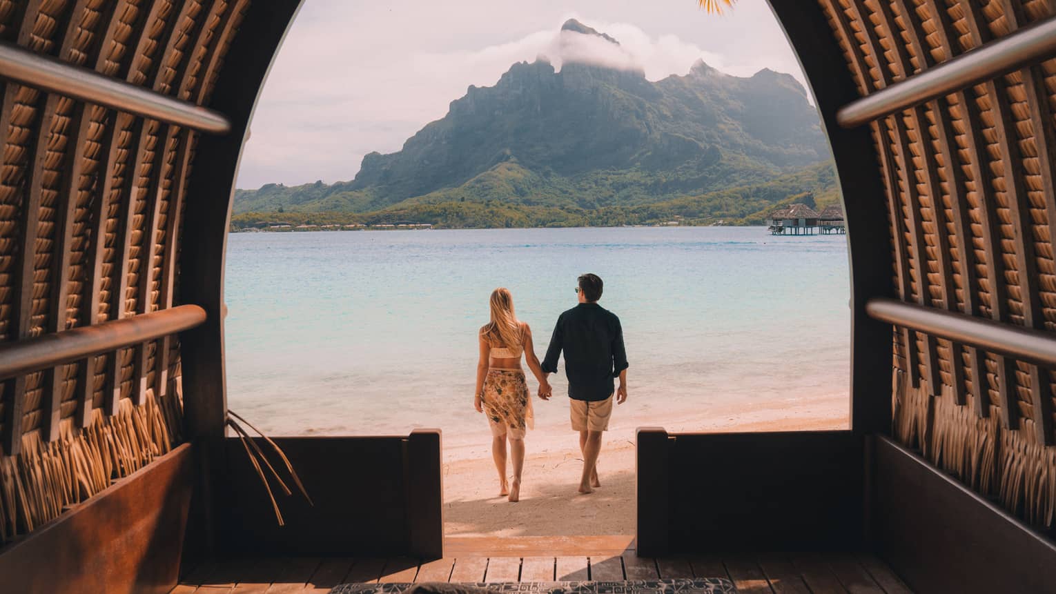 Man and woman on Bora Bora beach hold hands, look out to mountain