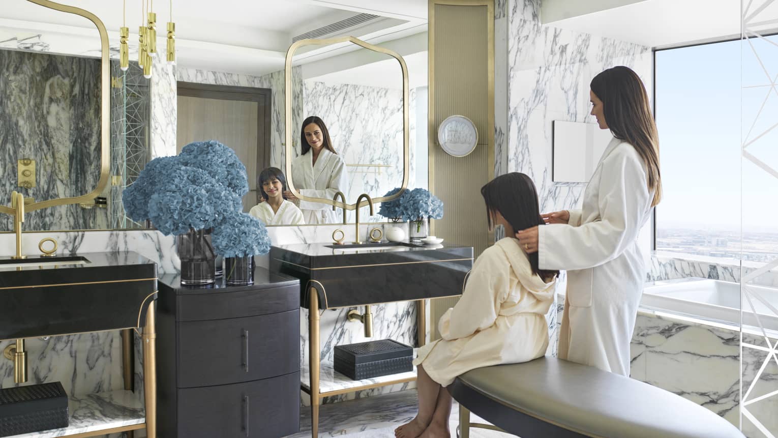 Woman and young girl in bathrobes sit in front of mirror in bathroom