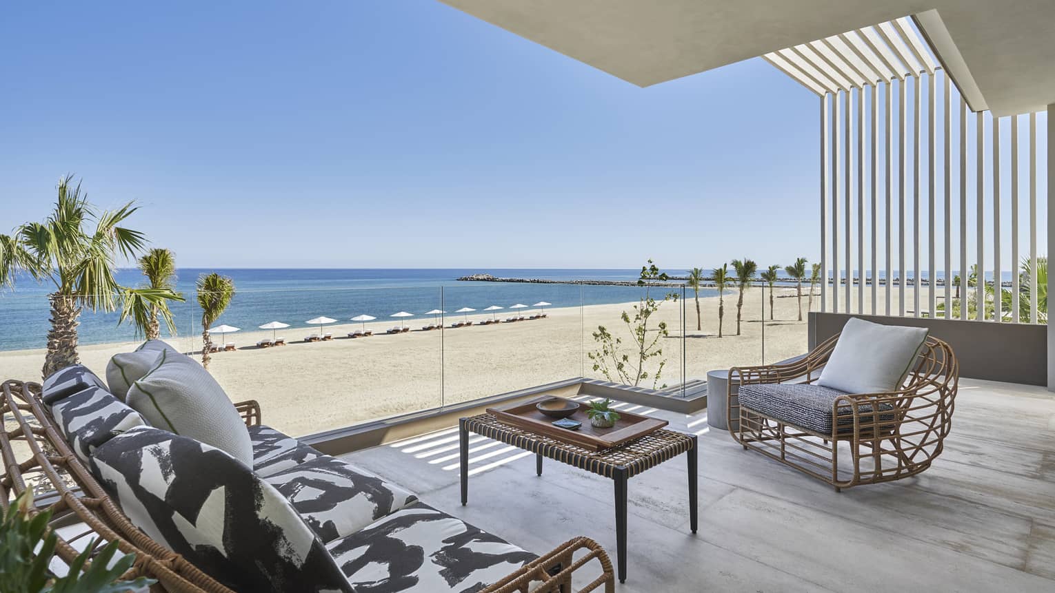 Outdoor terrace with modern wicker sofa and arm chair, glass railing, beach and ocean view