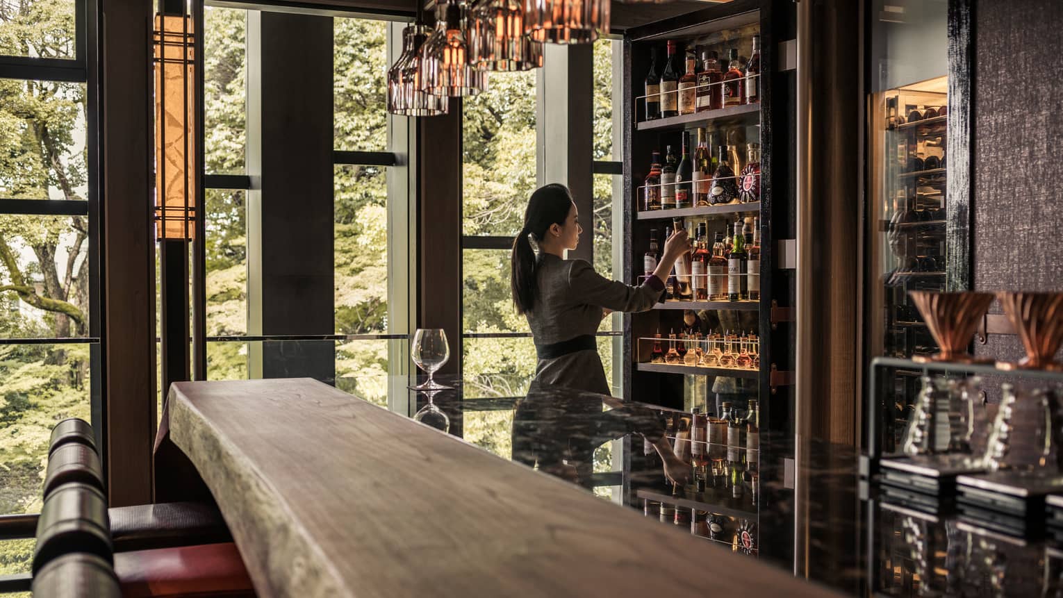Lounge bartender retrieves bottle on wine from cellar behind long rustic wood bar