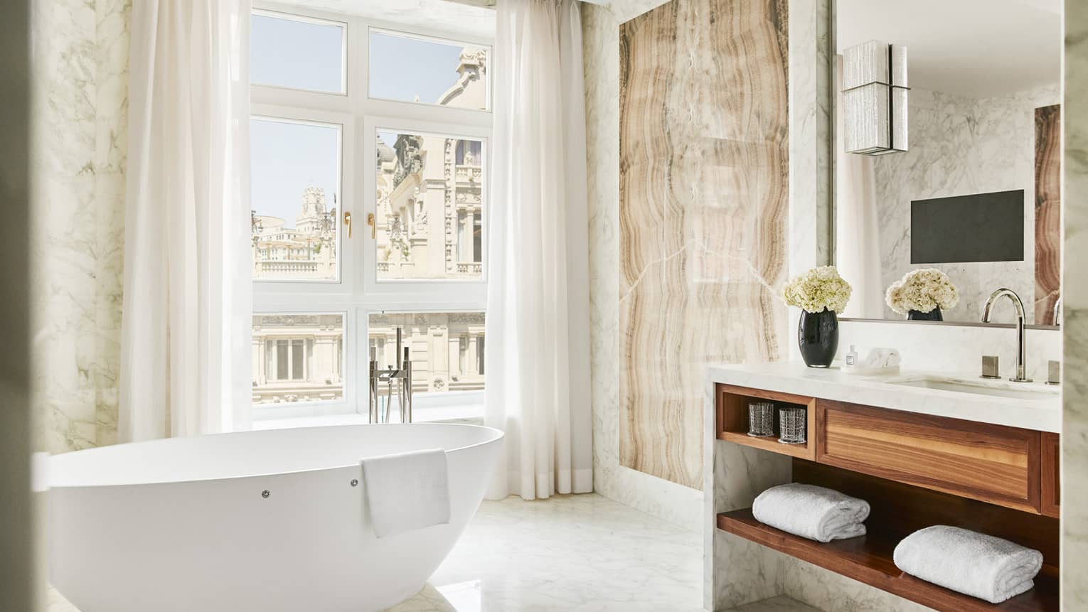 Bathroom with wall of windows, free-standing white tub, vanity with wooden shelves