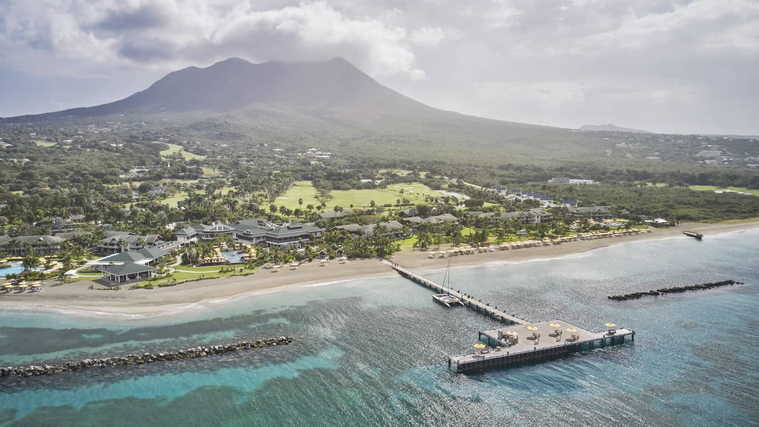 Aerial view of a resort property and dock on a beach shore with a mountain in the distance.