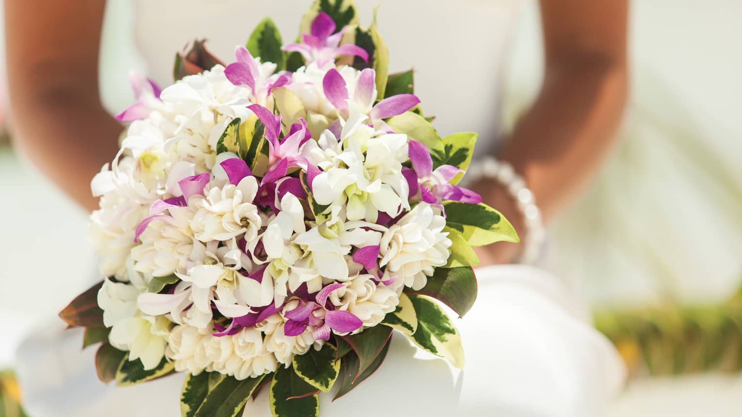Close-up of bride holding wedding bouquet with purple and white flowers