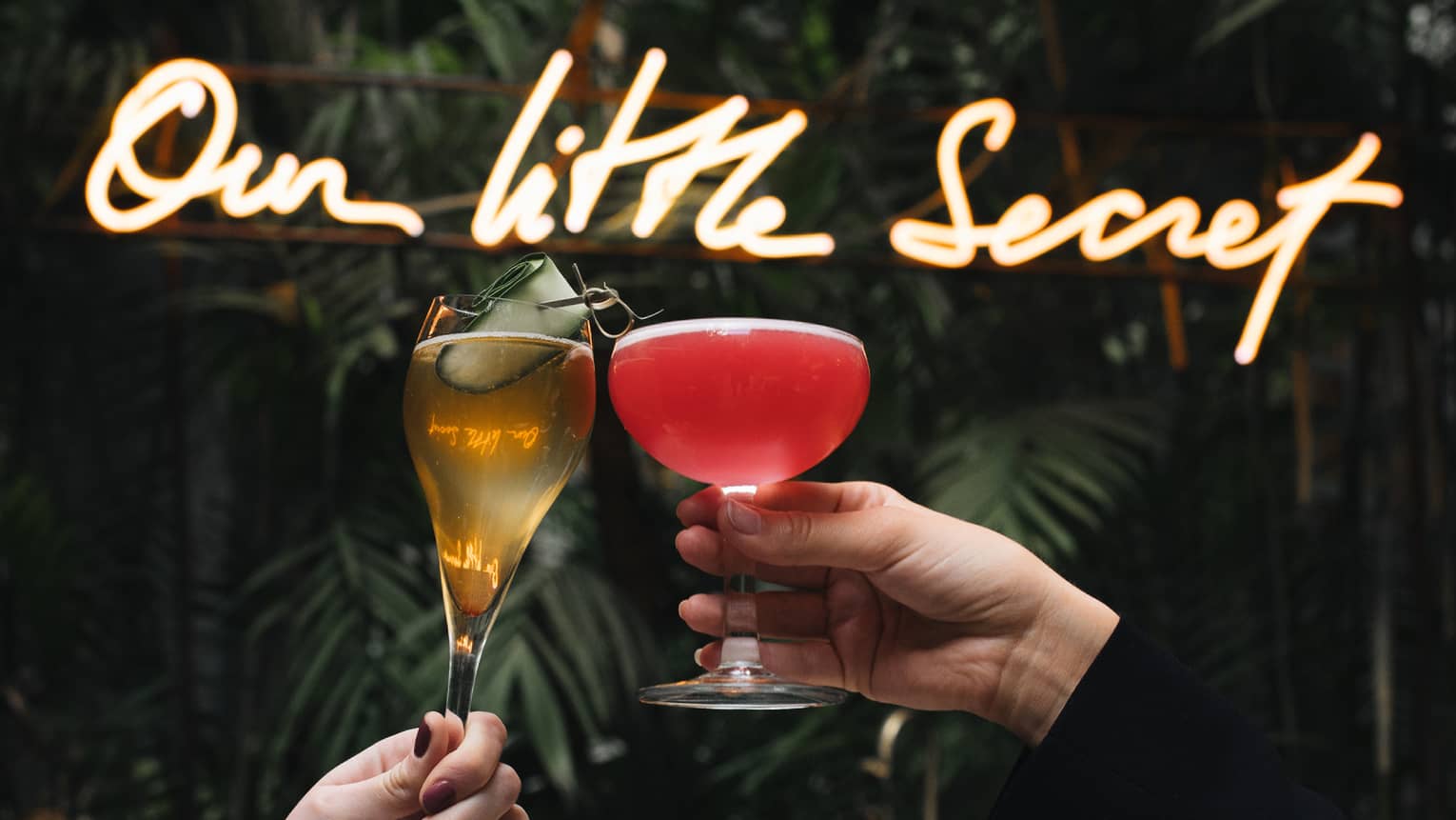 Two people toasting in front of a sign that says "our little secret."