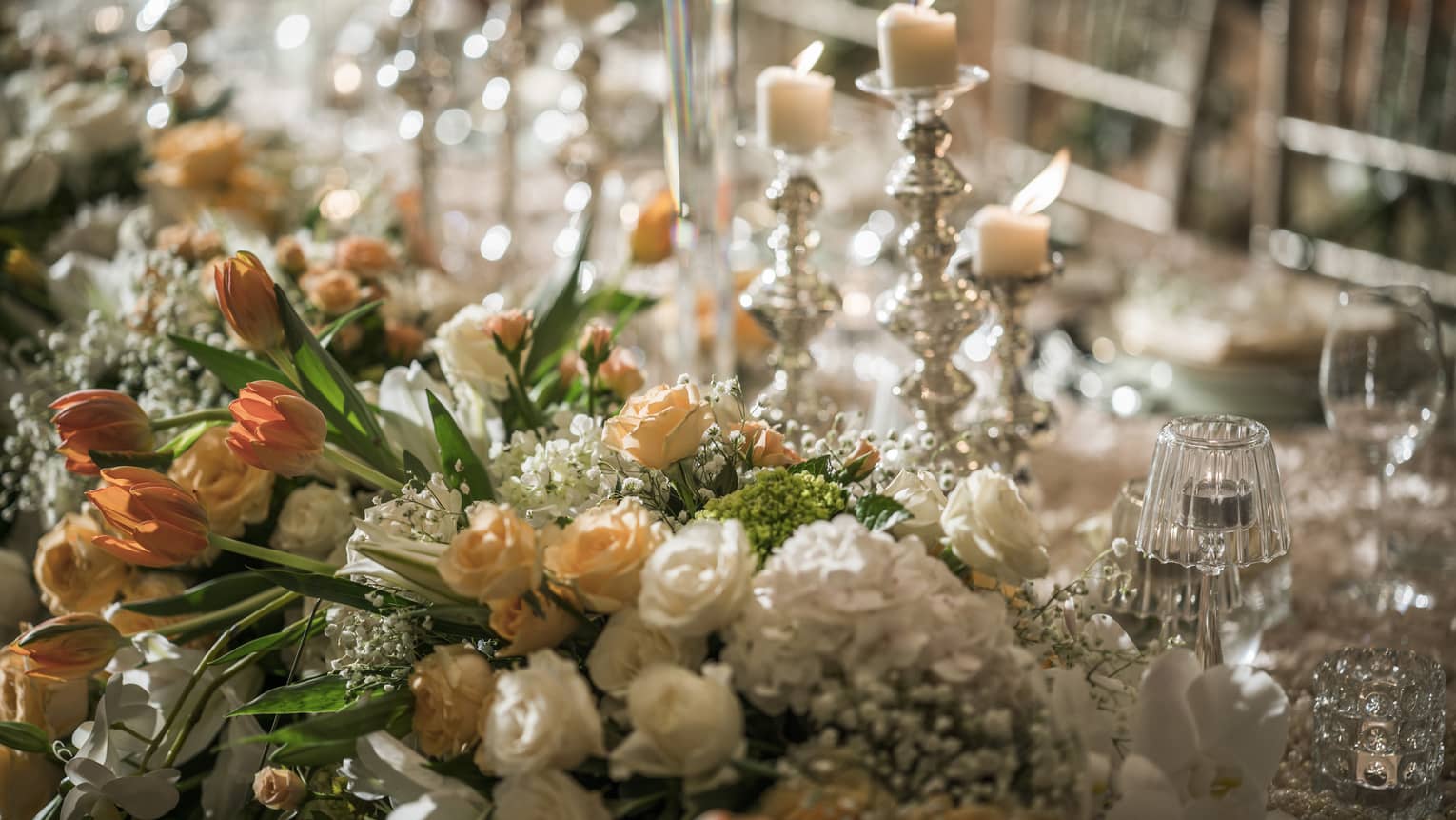 Close-up of flower arrangement with small white and peach roses, candles
