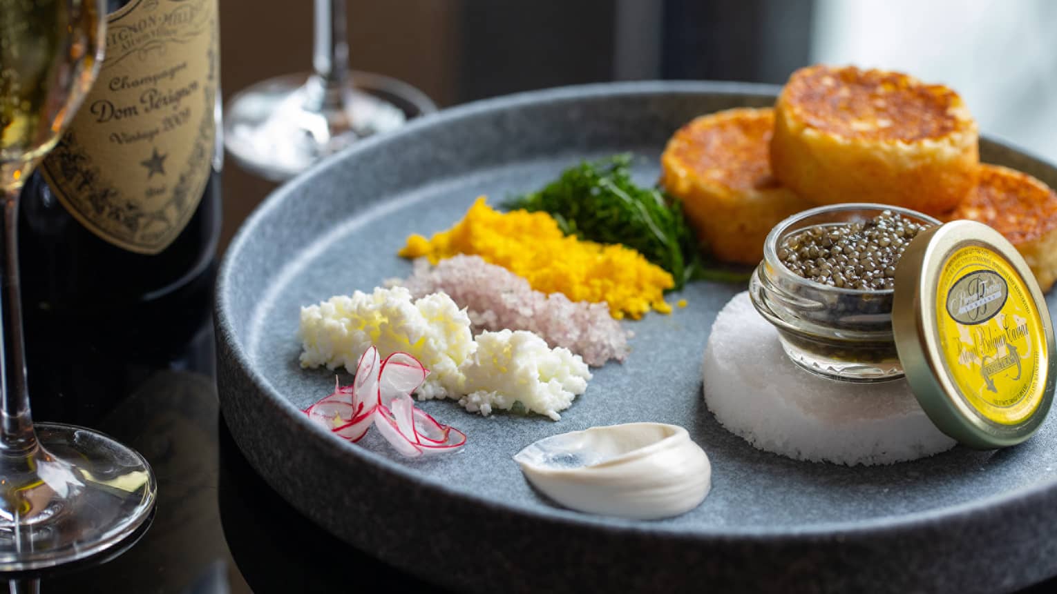 Caviar, seasonings, herbs, and potatoes on a grey plate.
