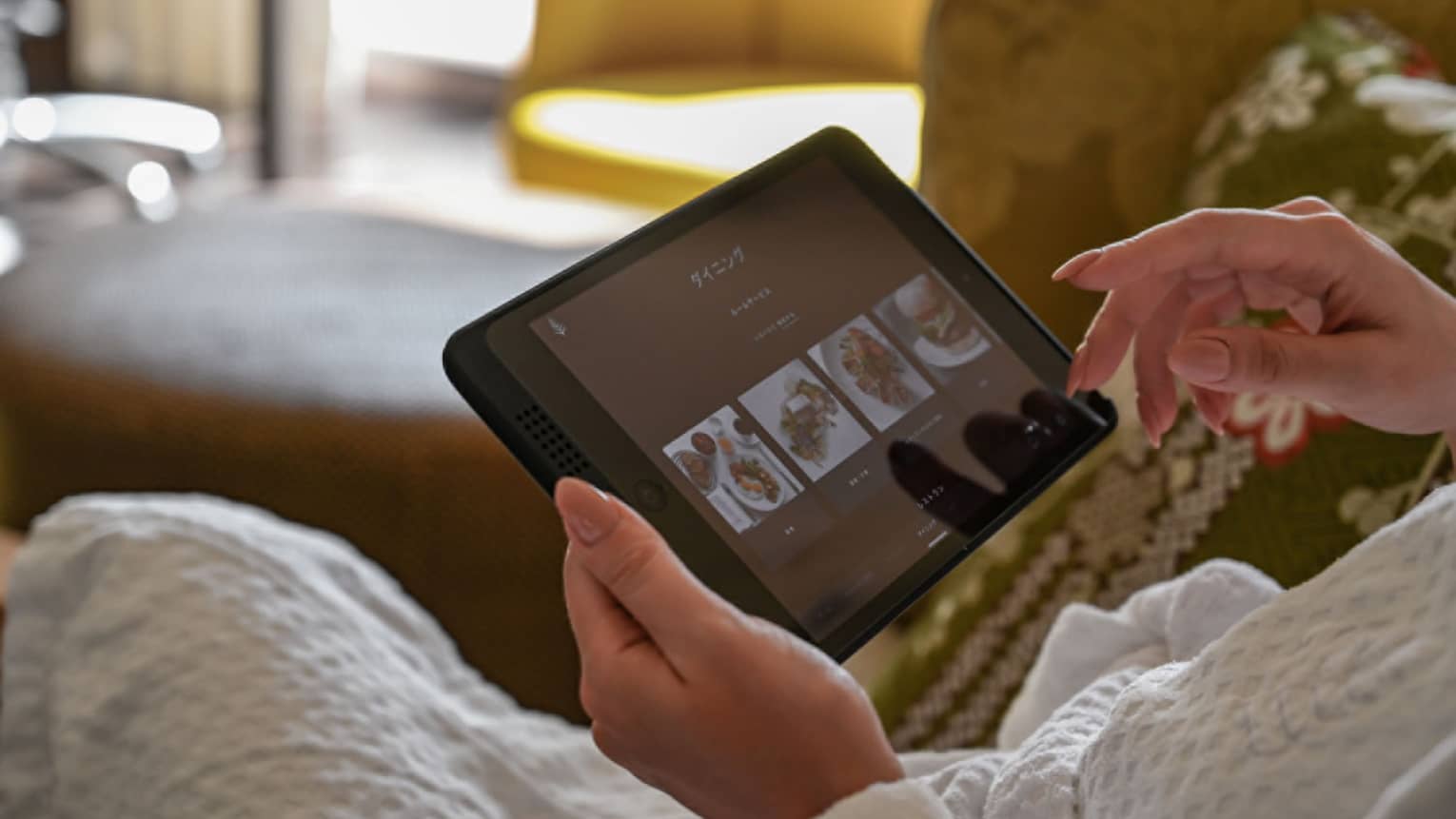 Person holding tablet and scrolling through in-room dining options in hotel room