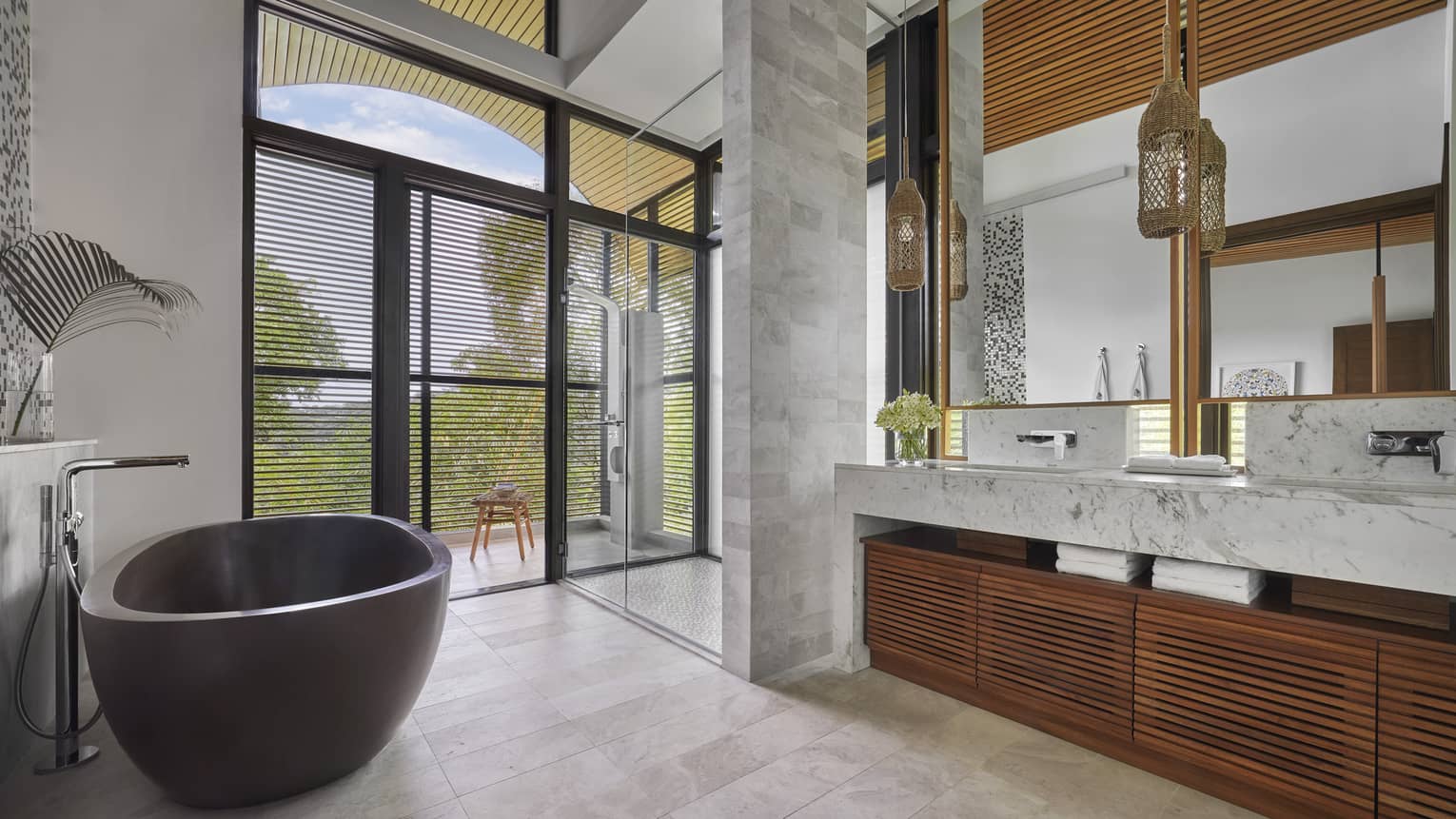 Bathroom with black standalone tub, marble and wood vanity, entrance to the outdoors