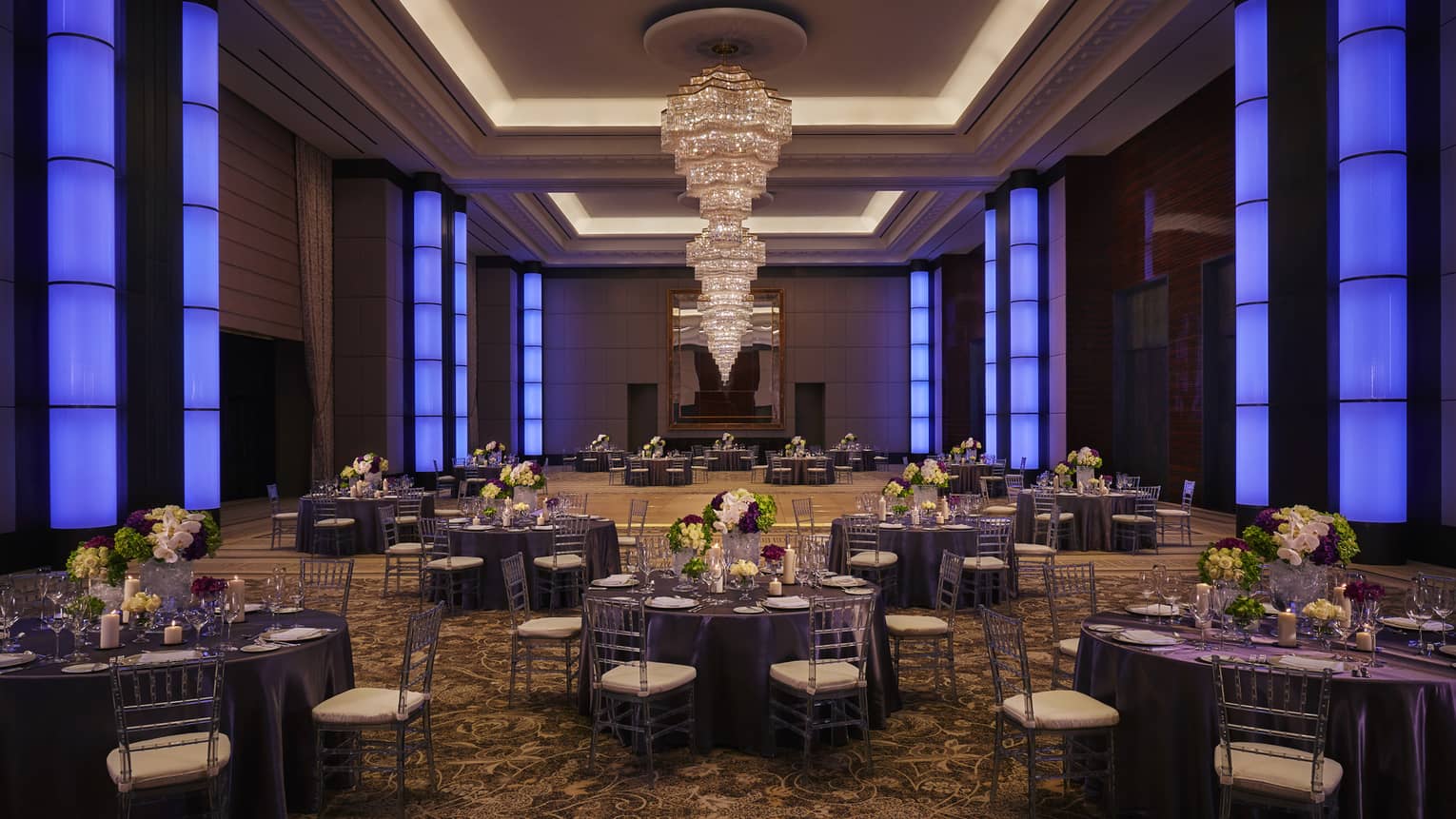 Round dining tables under large crystal chandelier in spacious ballroom