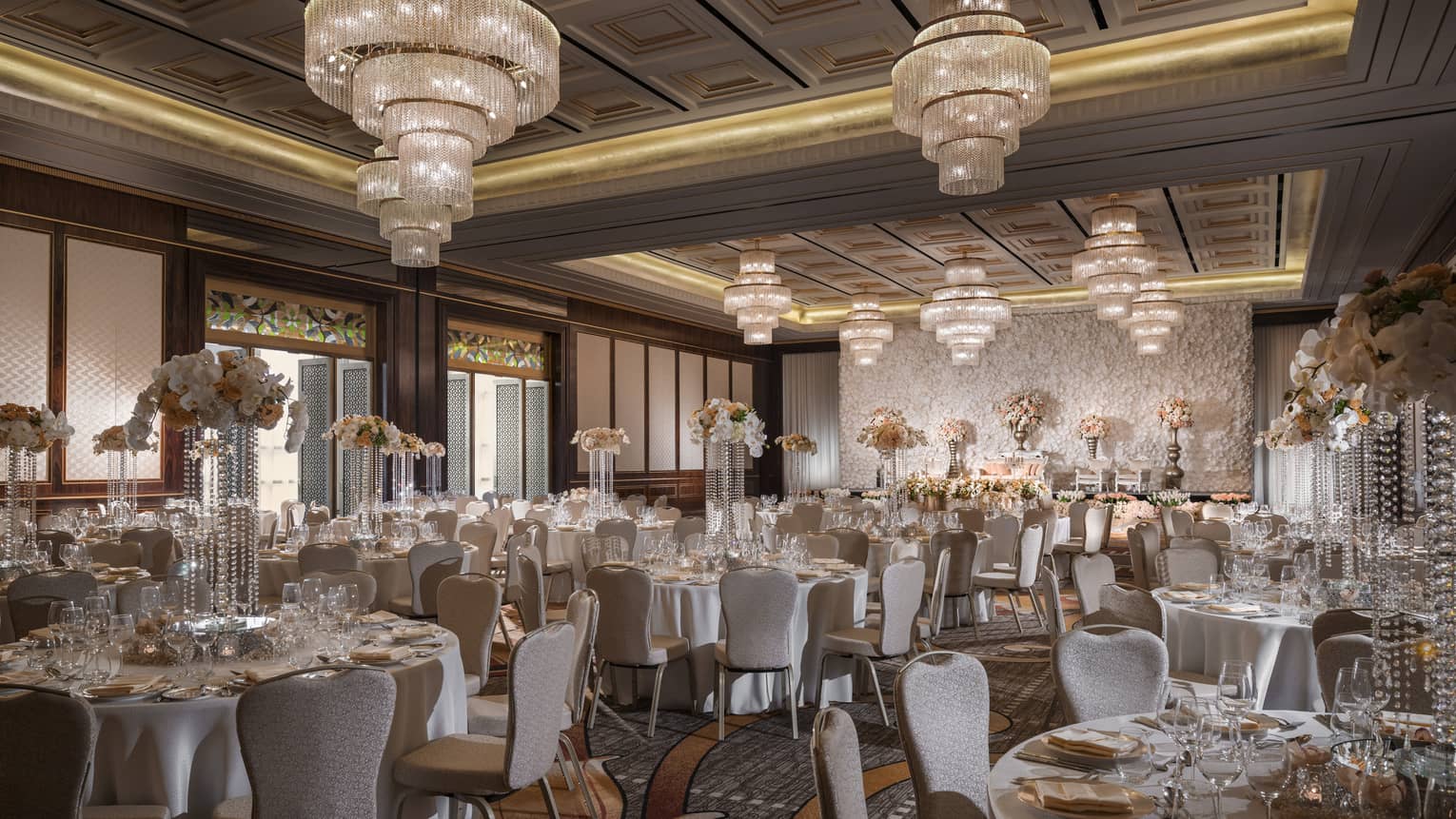 Large crystal chandeliers hang over round banquet tables in ballroom