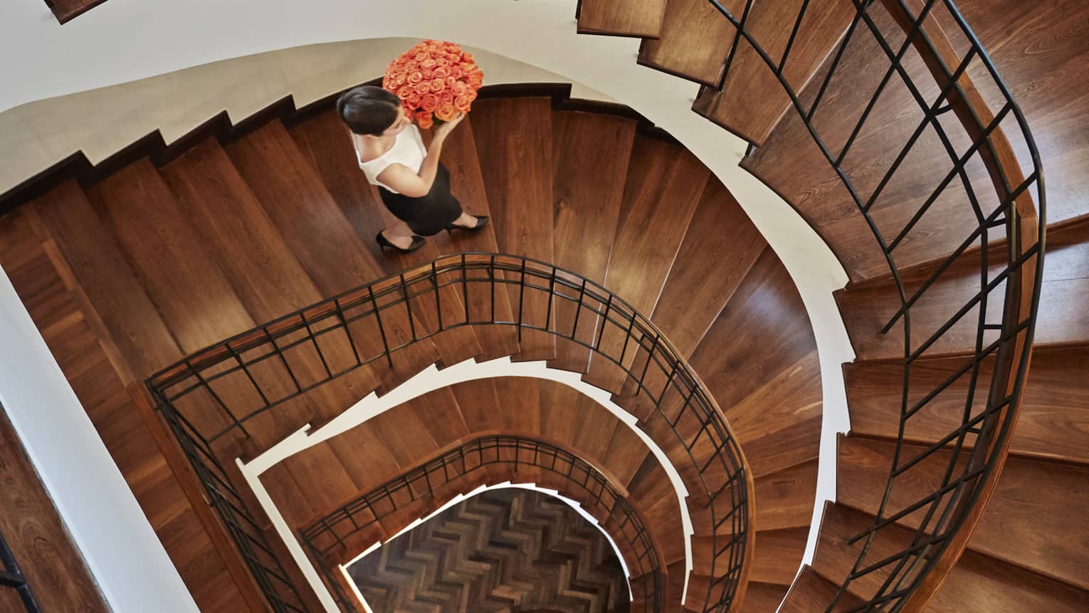 Aerial view of woman holding pink rose flower arrangement walking down wood spiral staircase