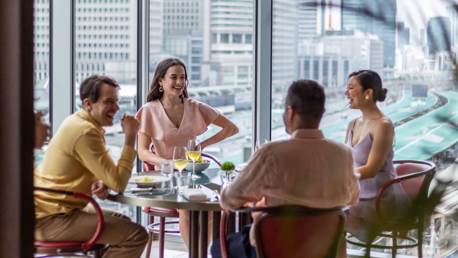 Two couples laugh and drink wine at Maison Marunouchi with views of the Shinkansen trains behind them