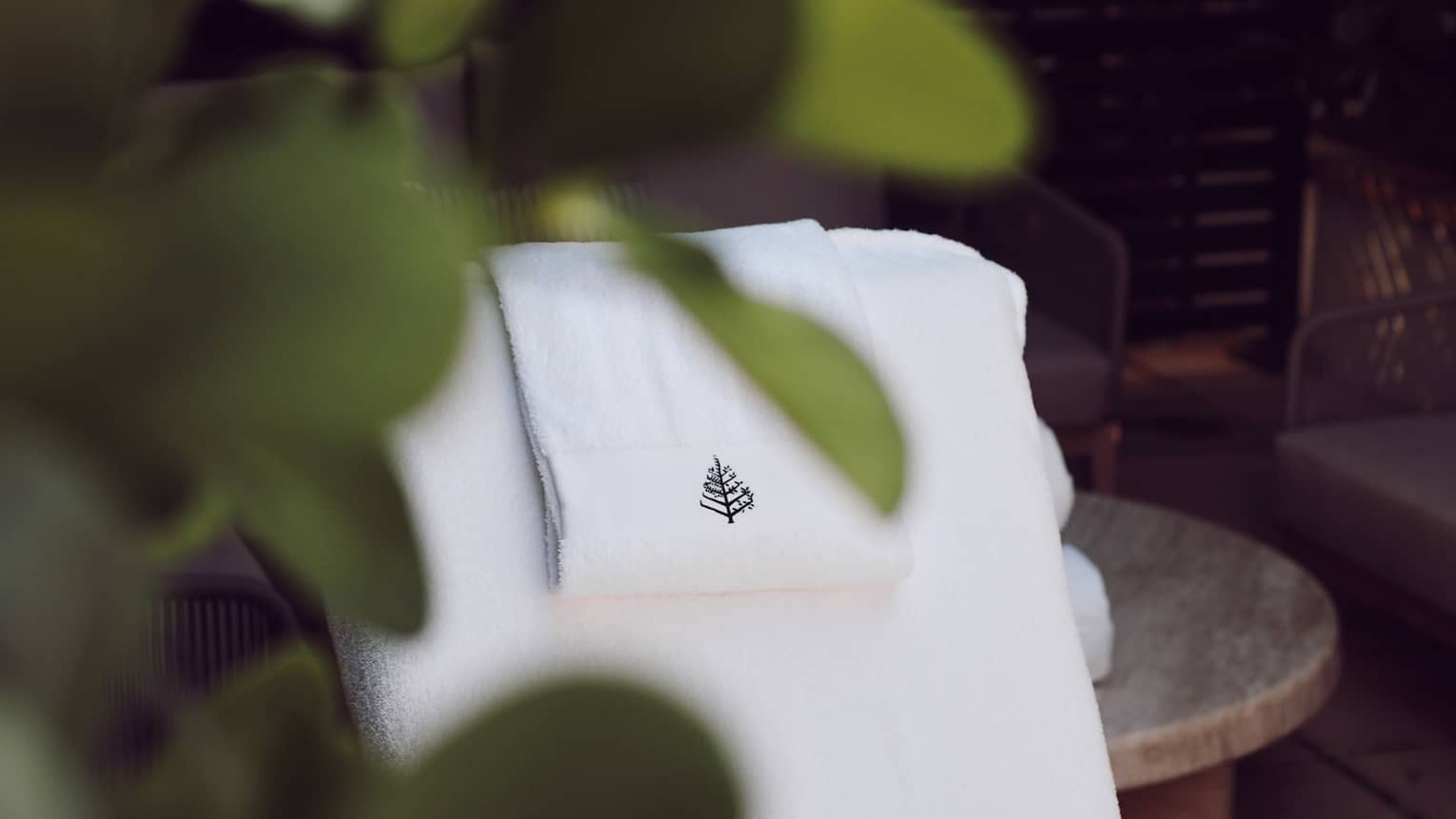 Vantage point from behind lush greenery of a white daybed draped with a white towel bearing the Four Seasons logo.