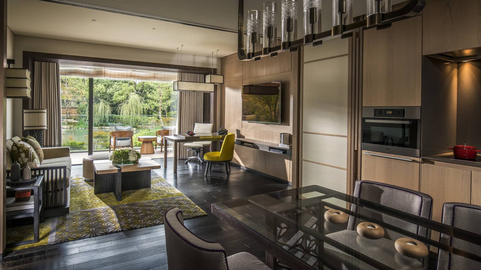 Long glass dining table under chandelier by living room, open wall to sunny patio