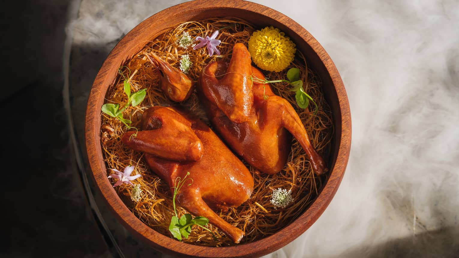 Spatchcocked pigeon in wooden bowl decorated with edible flowers