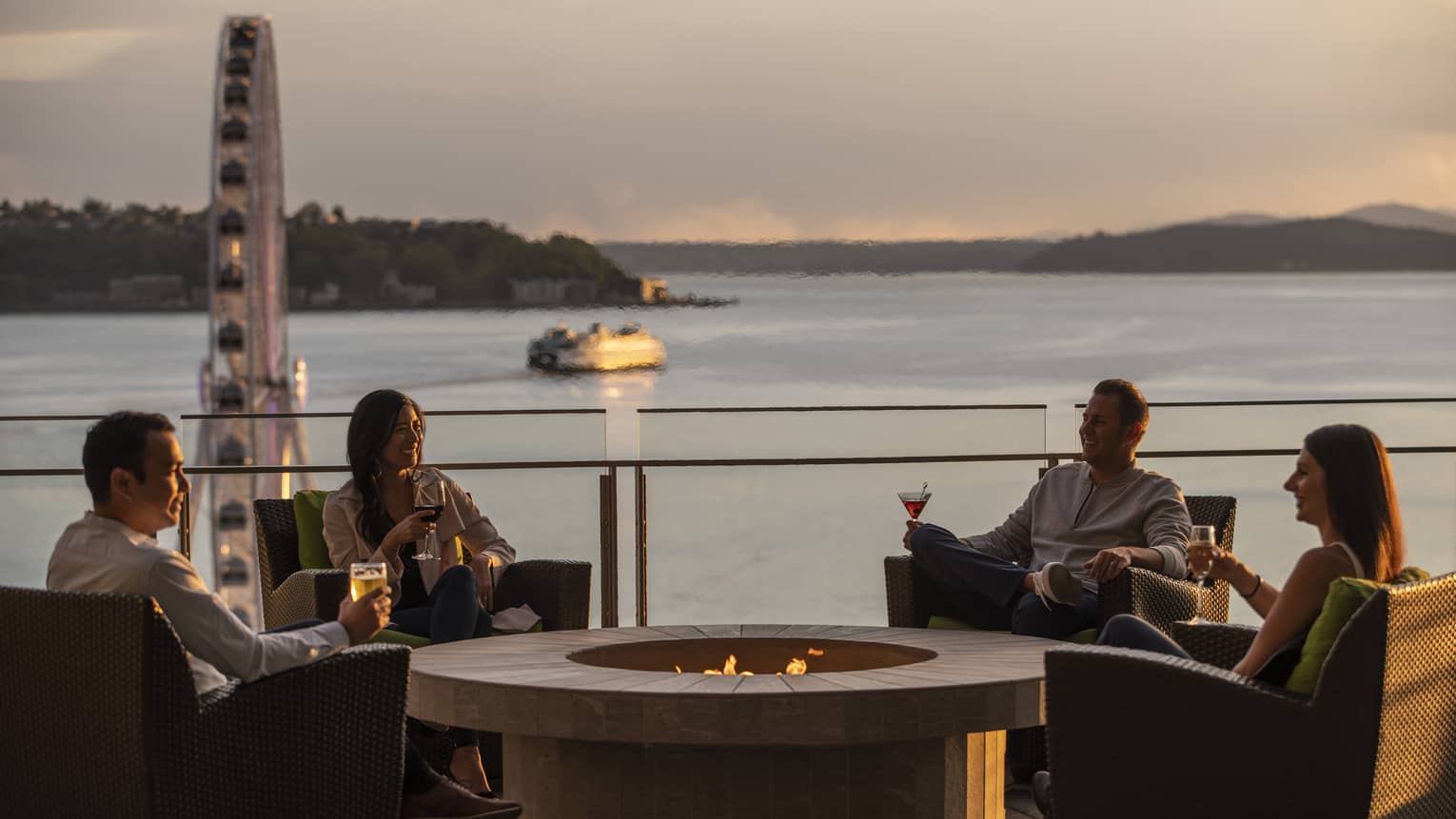 Guests enjoy drinks by the firepit with a view of the Seattle Great Wheel and bay behind them