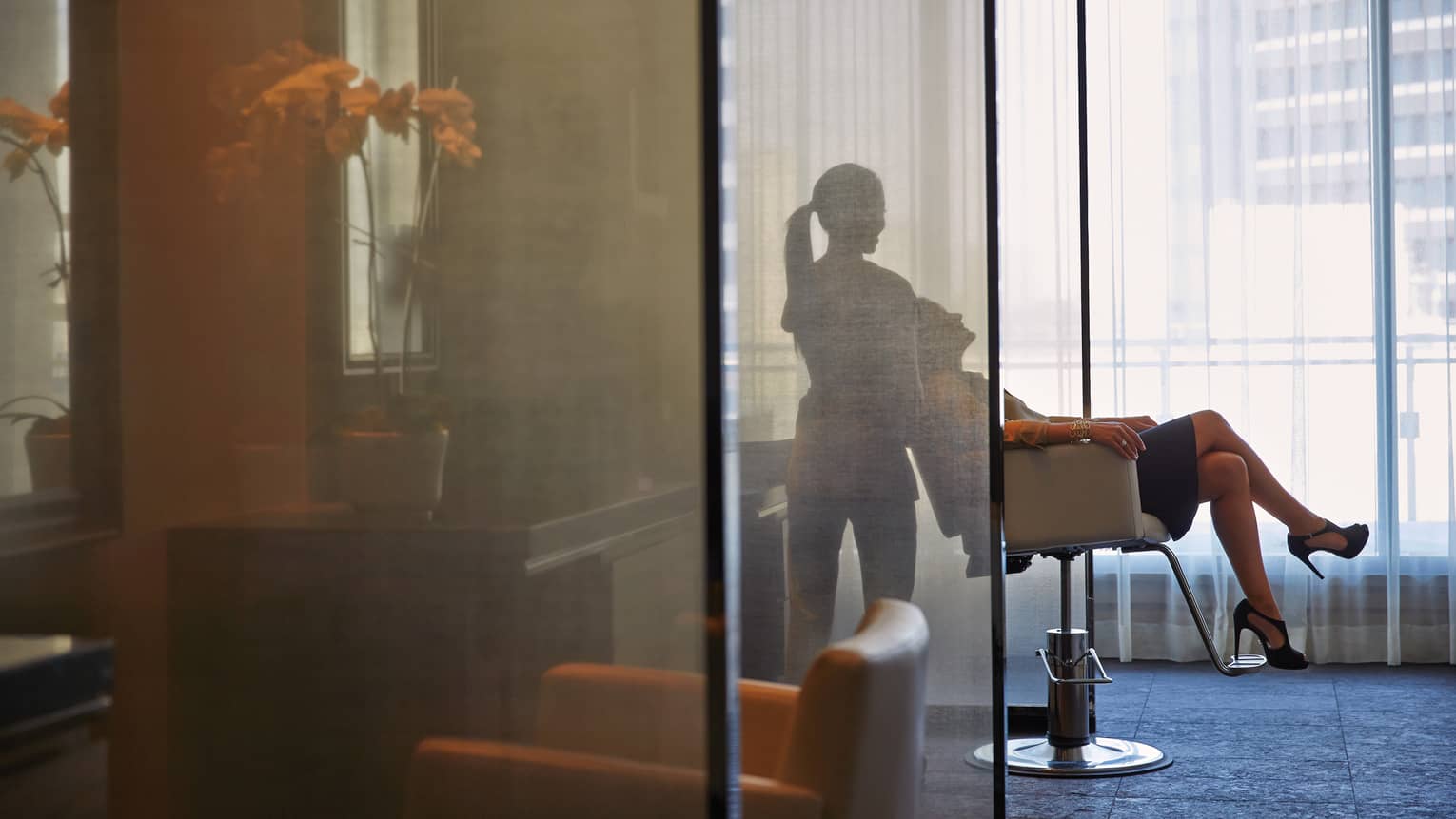 Silhouette of spa staff tilting woman back in salon chair behind sheer screen