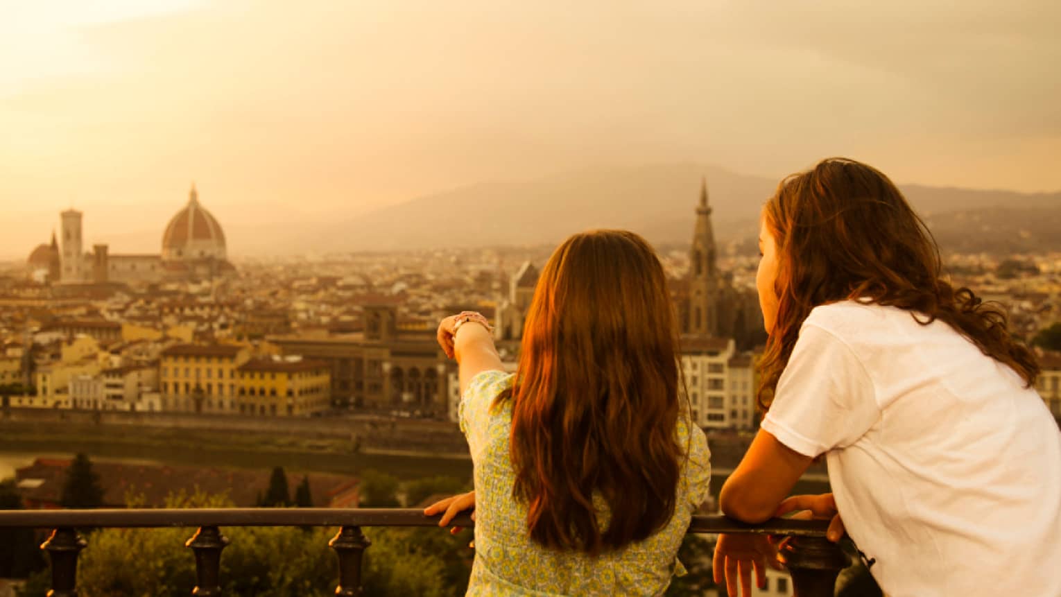 Back of two young girls looking out over Florence skyline, rooftops, Duomo at sunset