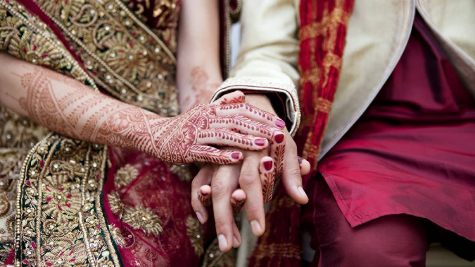 Indian wedding ceremony, bride with henna designs on arm holds groom's hands