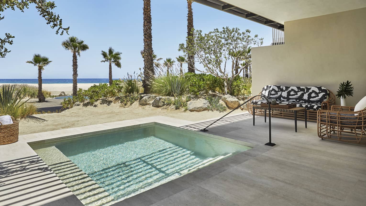 A small pool inside a suite that is open to a beach and palm trees outside.
