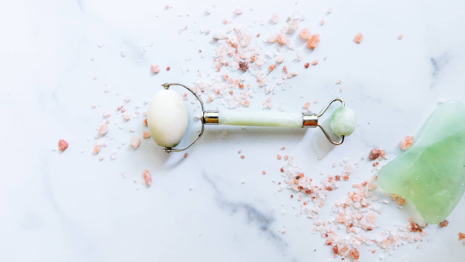 a spa roller tool on a white marble counter surrounded by himalayan salt