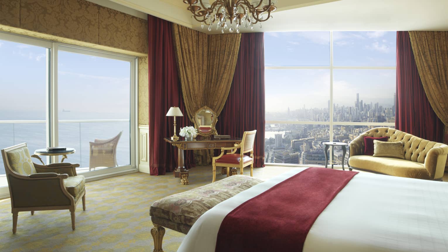 White bed with red suede sash, antique-style bench, green-and-gold leaf armchair, corner suite views of water and city