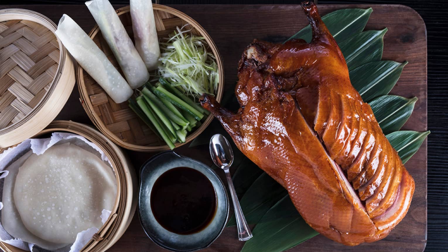 Aerial view of Peking Duck sliced on side, bamboo basket with spring rolls, onions