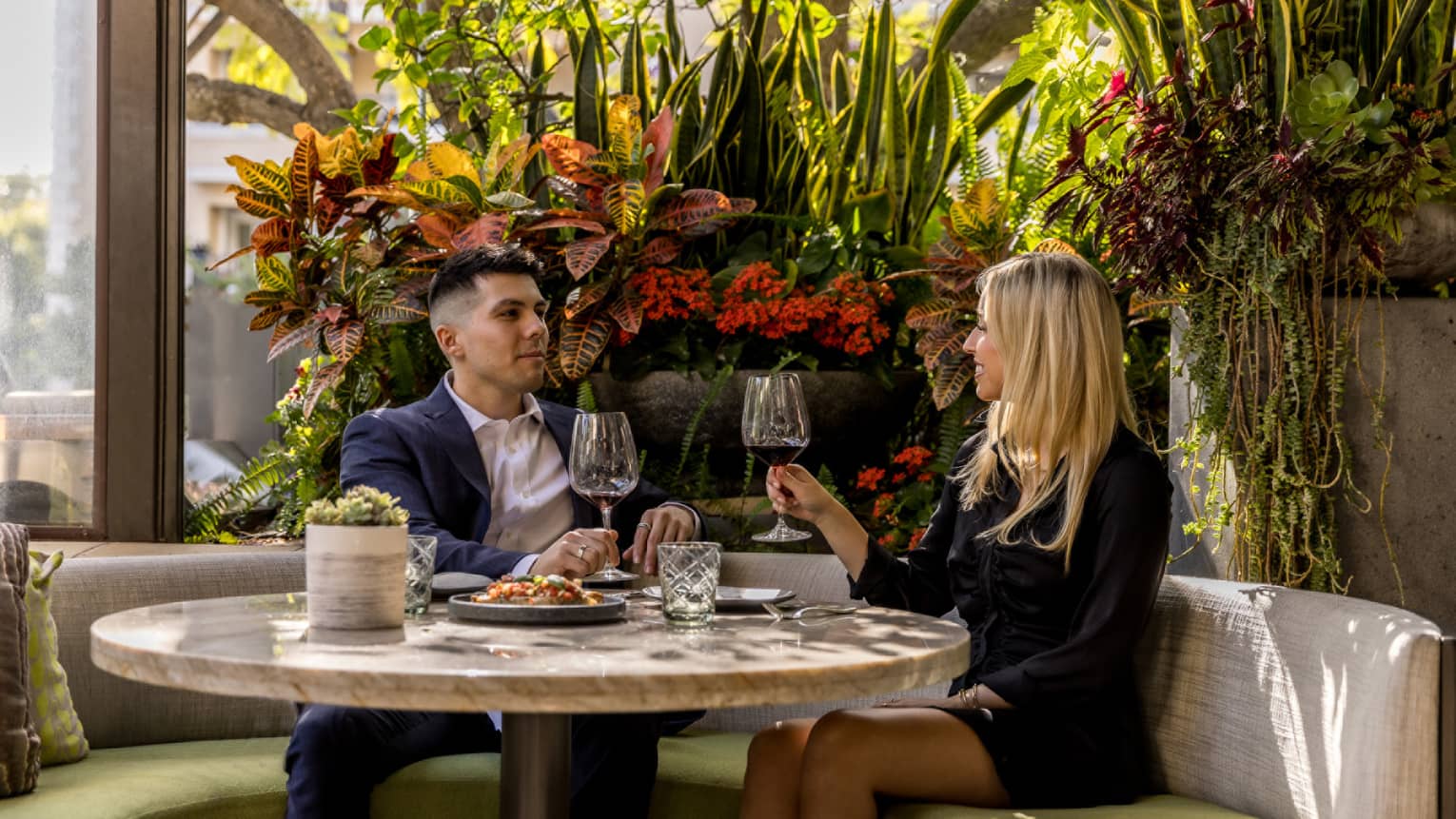 A man and woman sitting near flowers drinking wine.