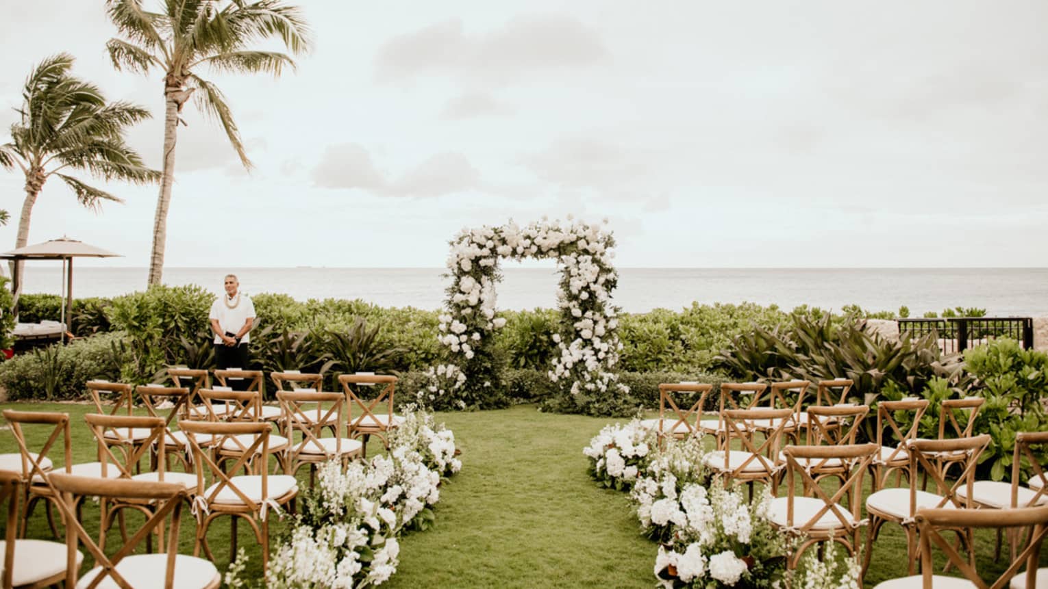 An outdoor wedding venue near the ocean, with wood chairs and flowers along a path.