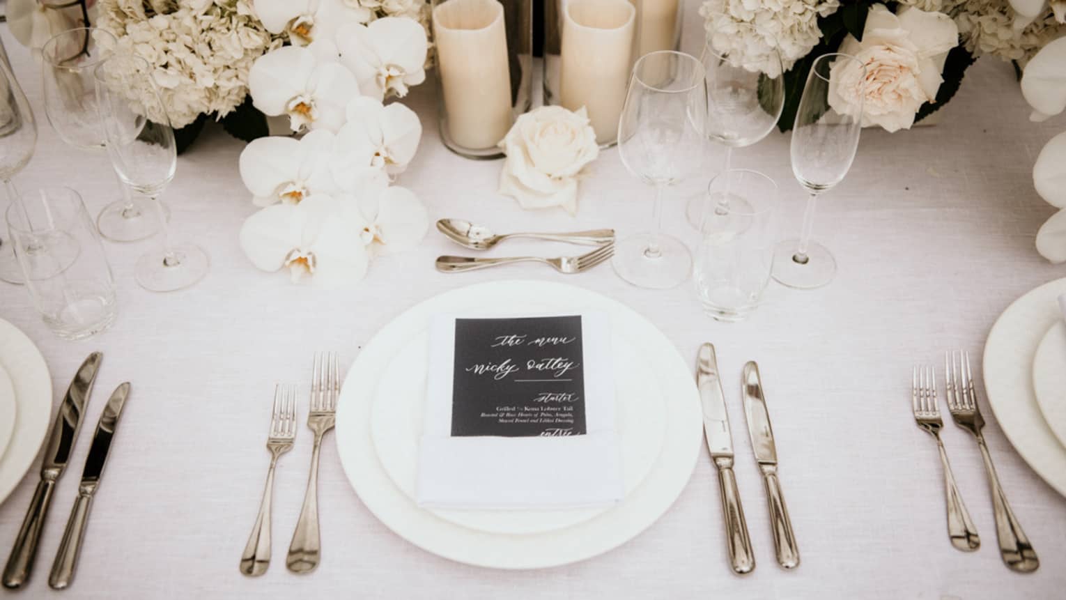 Wedding table setting with white flowers and candles, menu on white napkin and plates