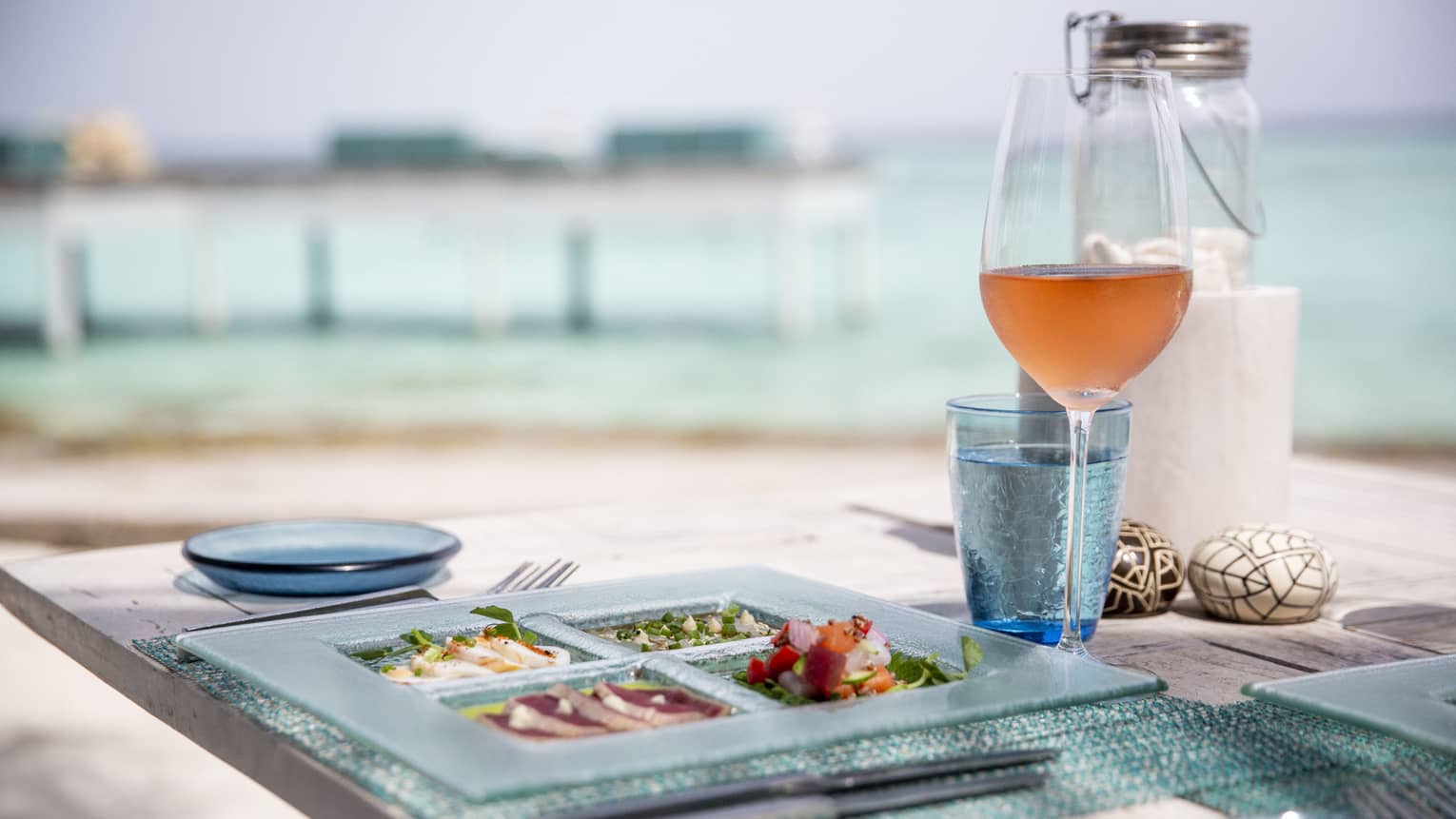 Outdoor dining table with glass plate with sashimi, wine overlooking lagoon