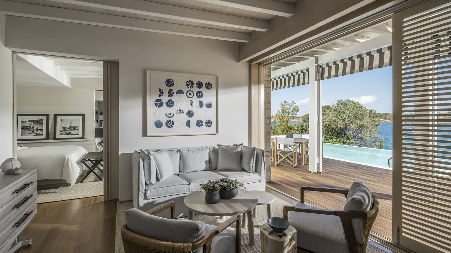 Living area with three-seat grey sofa and two arm chairs opens up to private deck with pool