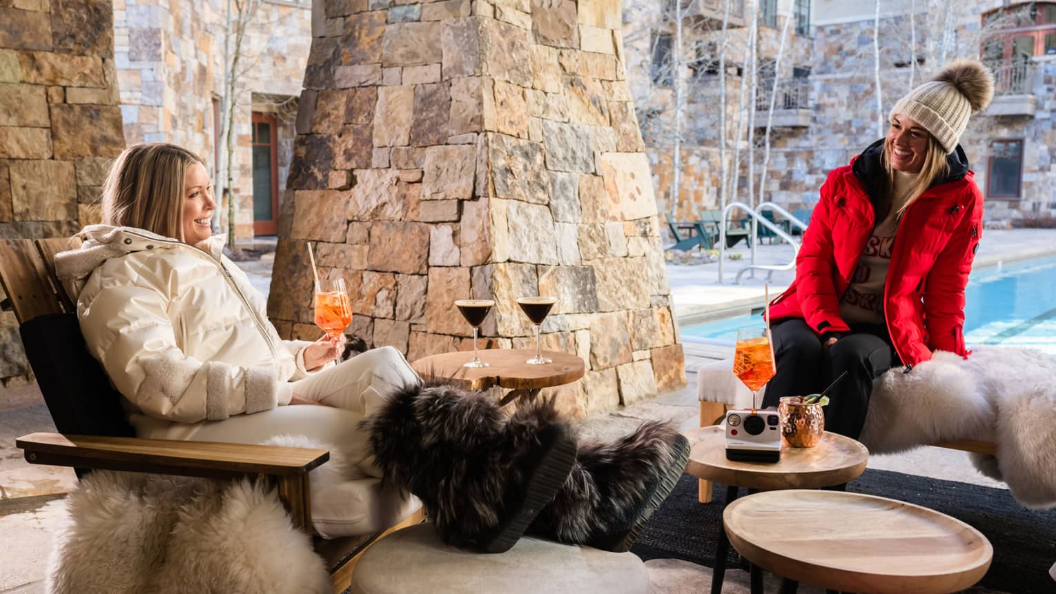 Two guests sitting in chairs near the pool wearing coats.