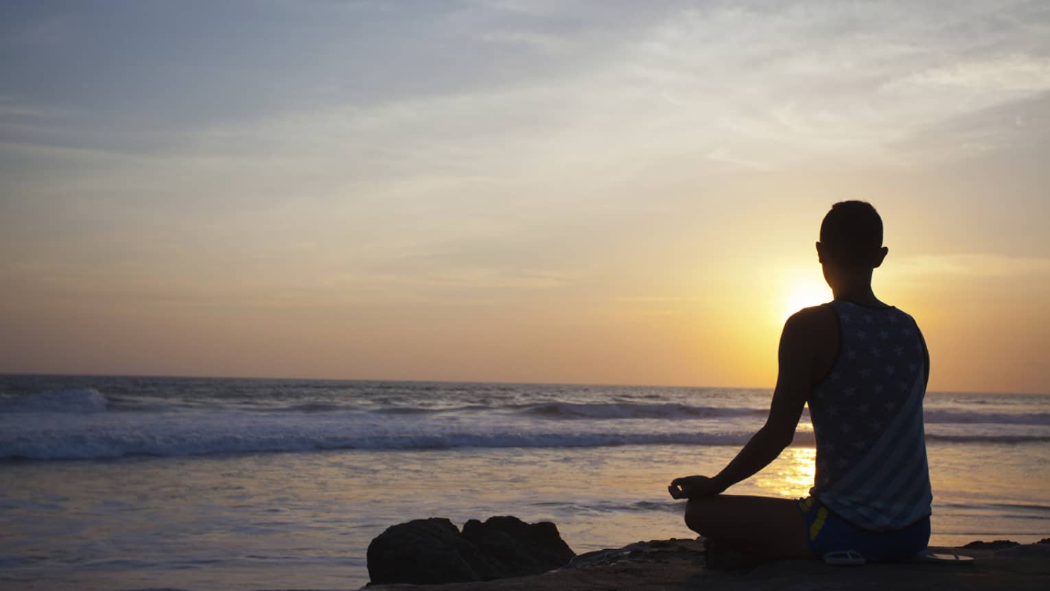 Silhouette of person sitting cross-legged, meditating in front of beach at sunset