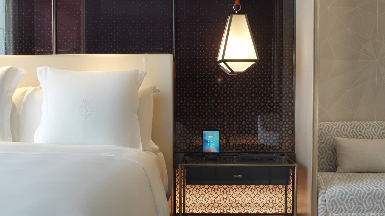 Close-up of modern lantern hanging above nightstand beside white pillow, bed