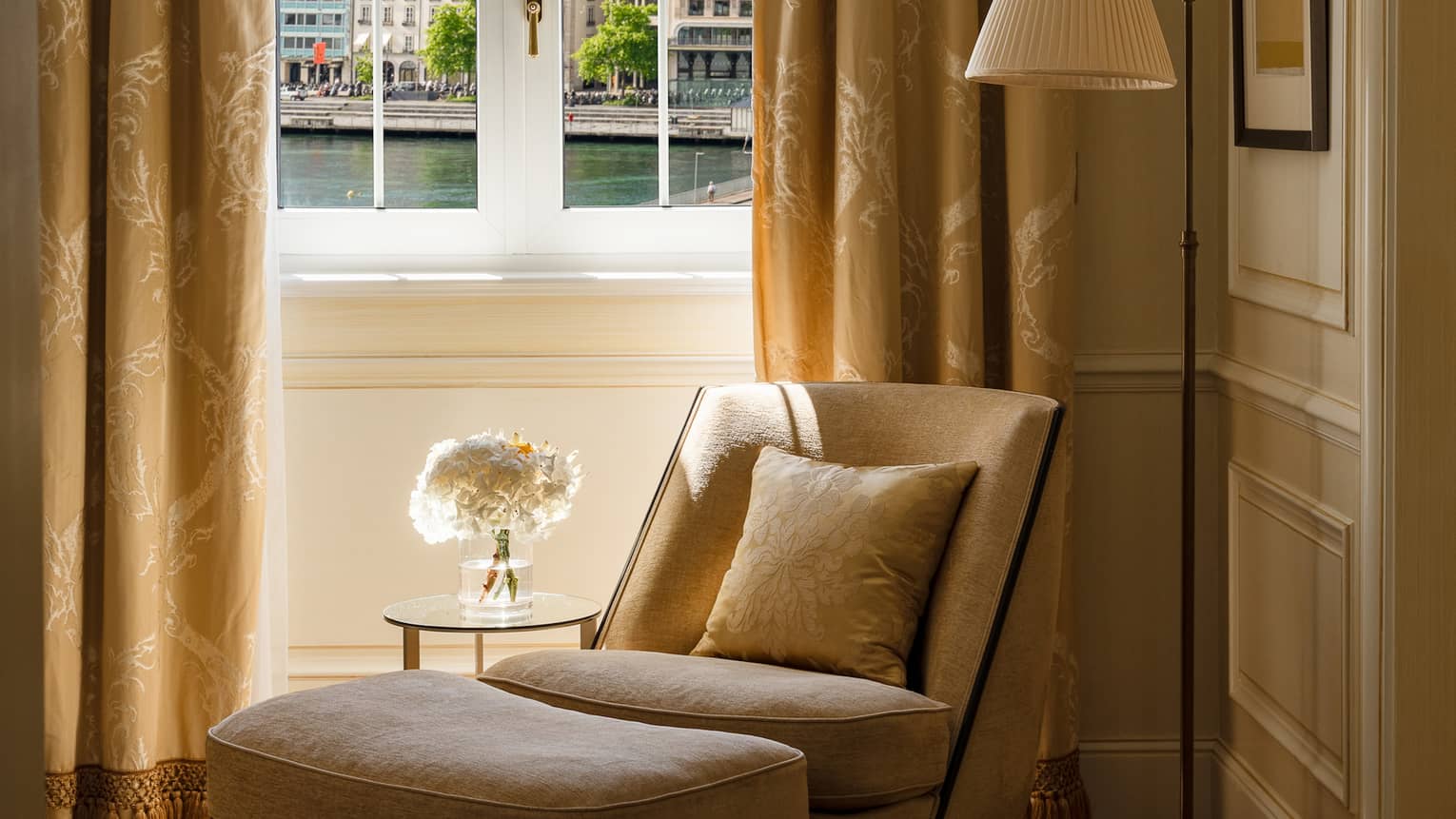 Corner of a luxury suite, where an arm chair and ottoman sit beside a window, at Four Seasons Hotel des Bergues, Geneva