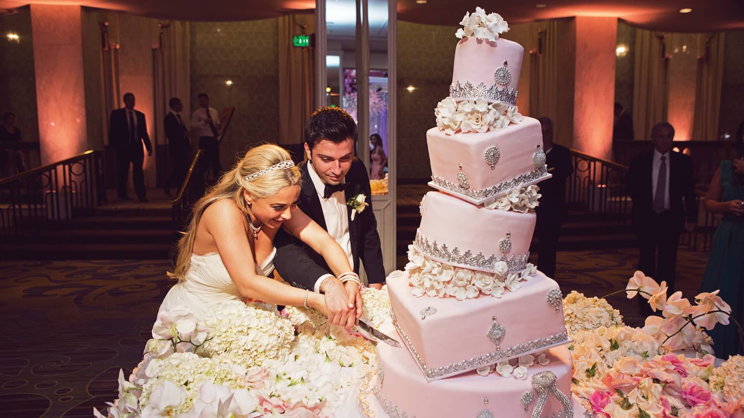 Bride and groom cut large, five tiered pink layer cake at wedding reception